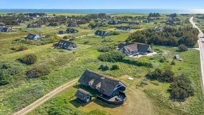 Une vue aérienne d’une zone rurale avec plusieurs maisons aux toits de chaume, un chemin de terre et une étendue d’eau en arrière-plan.