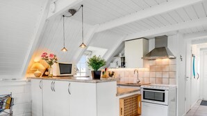 Une cuisine moderne avec des meubles blancs, un îlot central, des luminaires suspendus et une cuisinière visible.