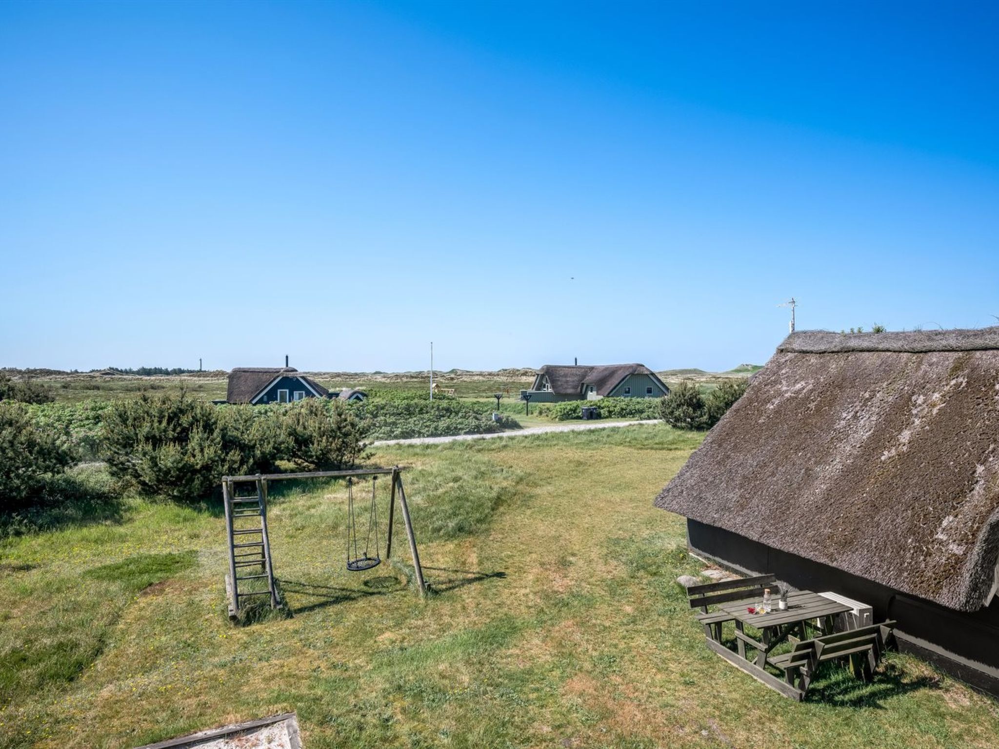 Paesaggio rurale con una casa a tetto di paglia, un'altalena e due altre case sullo sfondo.