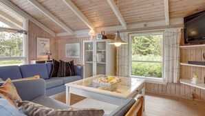 A cozy cabin interior with a wooden ceiling, a blue sofa, a glass-top coffee table, and a television on a wooden shelf. - "Alfi" - 150m from the sea by Interhome (Sæby)