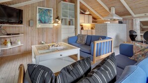 A cozy loft-style living space with a high ceiling, wooden beams, a television, a painting, a kitchenette, and a comfortable seating area with a sofa and cushions. - "Alfi" - 150m from the sea by Interhome (Sæby)