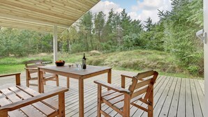 Eine Holzterrasse mit Tisch und Stühlen, umgeben von einer bewaldeten Landschaft.