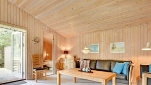 Ein gemütliches Zimmer mit Holzwänden, Holzbalkendecke, einer Couch, einem Tisch und einem Sessel.