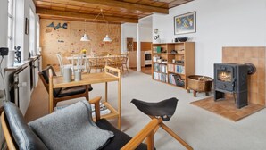 A cozy living room with a wooden ceiling, a dining area with chairs and a table, a bookshelf, and a fireplace. - "Scarlet" - 5m from the sea by Interhome (Hasle)