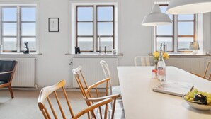 A dining area with a white table, wooden chairs, pendant lights, and a view of the sea through large windows. - "Scarlet" - 5m from the sea by Interhome (Hasle)