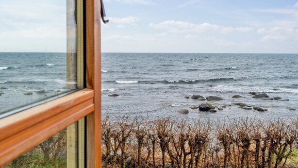 A view through a window with a wooden frame and a black handle, overlooking a rocky shoreline with sparse vegetation. - "Scarlet" - 5m from the sea by Interhome (Hasle)