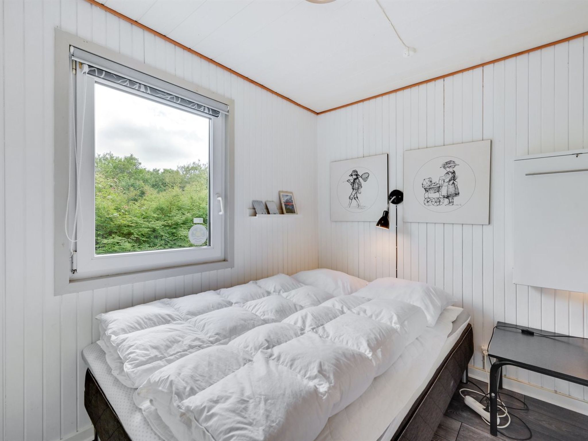 A bedroom with a bed, a window, and two framed pictures on the wall.
