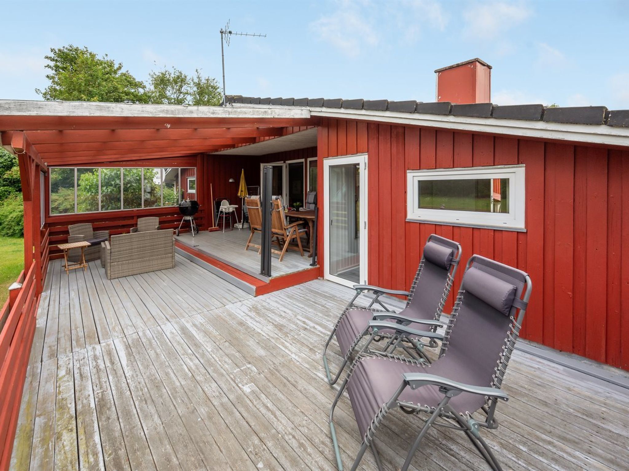 Une terrasse en bois rouge, meublée pour l’extérieur, dotée d’une porte-fenêtre coulissante et d’une petite fenêtre.