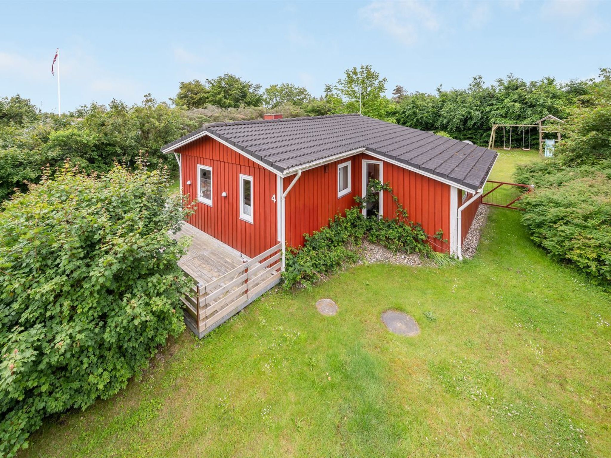 A red wooden cabin with a sloped roof, a wooden deck, and a swing set in the background.