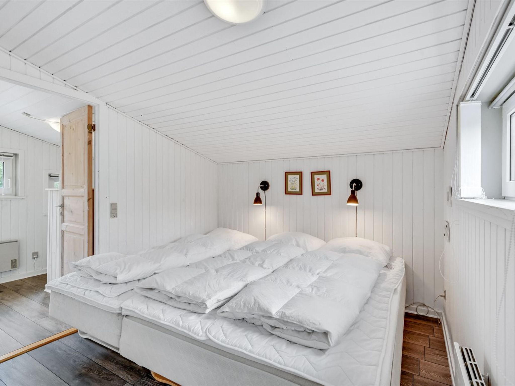 A bedroom with a large bed, white walls, and wooden flooring.