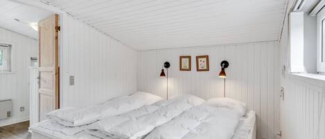 A bedroom with a large bed, white walls, and wooden flooring.
