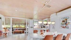 A modern dining area with a wooden ceiling, white walls, and a large table with chairs. There is a kitchen area visible through an open door. - "Anline" - 900m to the fjord by Interhome (Tarm)