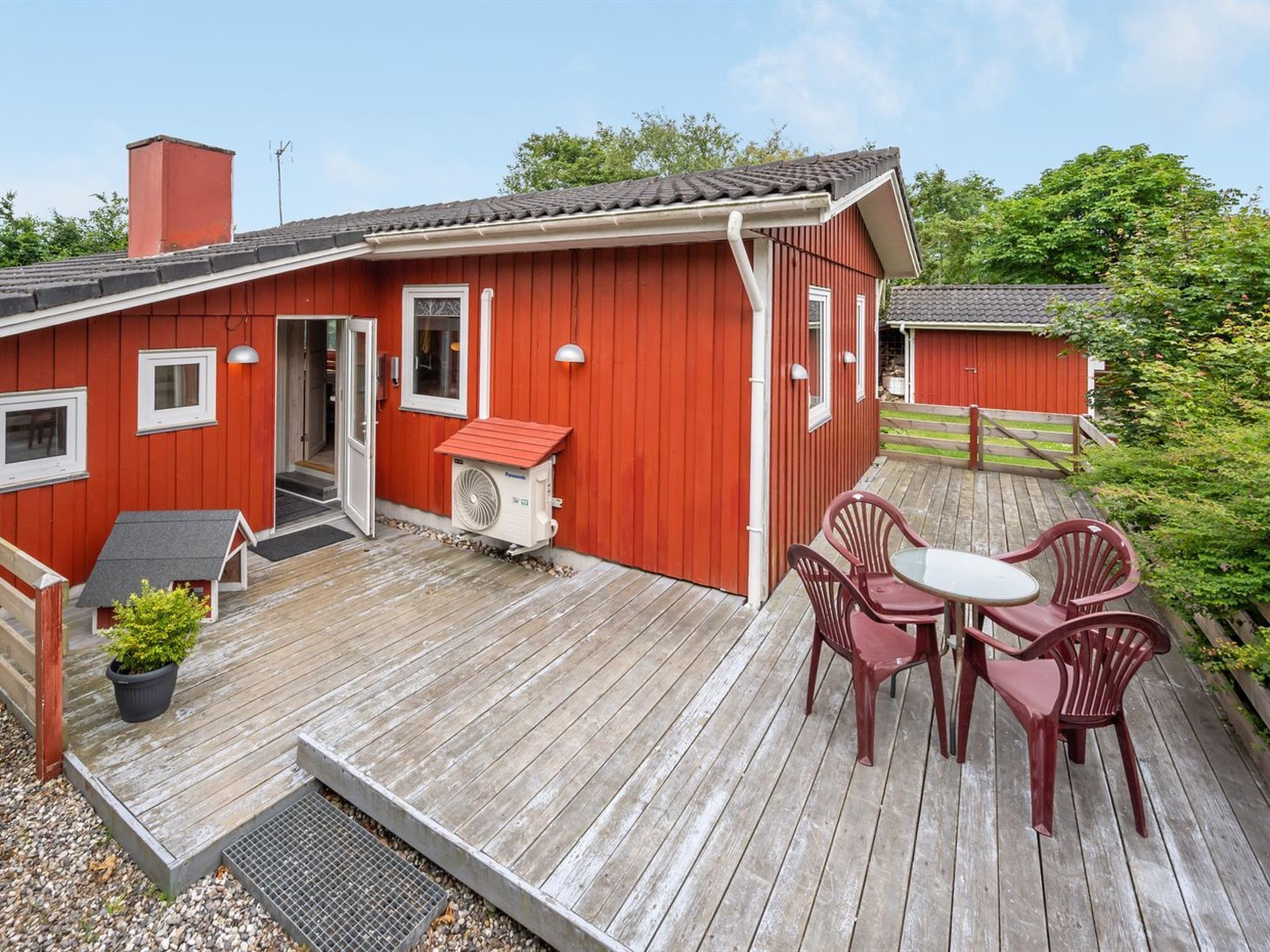 Una casa in legno rossa con una veranda, un piccolo tavolo e sedie, e una ventola.
