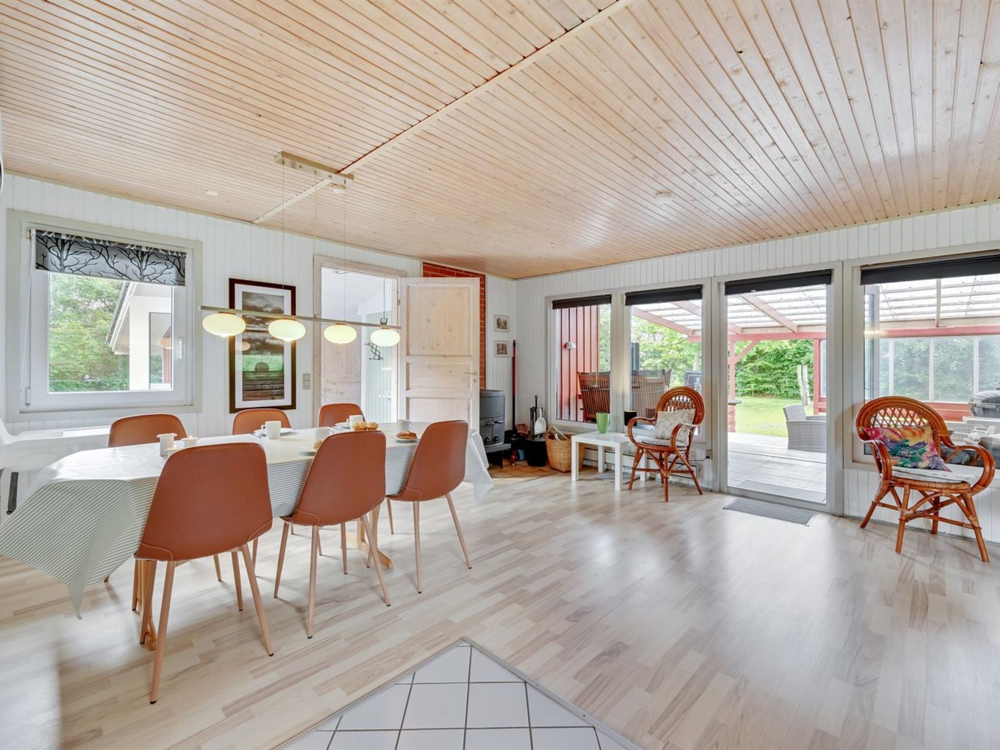 A spacious dining area with a wooden ceiling, large windows, and a view of the outdoors.