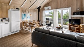 A modern kitchen with white cabinets, a dining area with wooden chairs, a gray sofa, and a television.