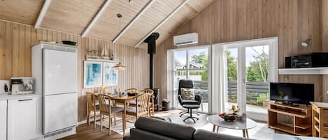 A modern kitchen with white cabinets, a dining area with wooden chairs, a gray sofa, and a television.