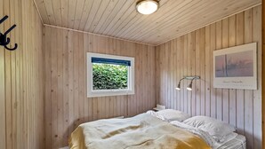 A bedroom with a bed, a window with a view of greenery, a wall-mounted light, and a framed picture.