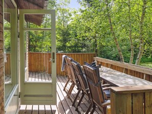 Une terrasse ouverte avec des chaises et une table en bois, entourée d’une clôture en bois et d’une végétation luxuriante.
