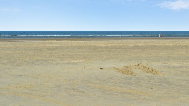 A wide sandy beach with a clear sky and calm sea.