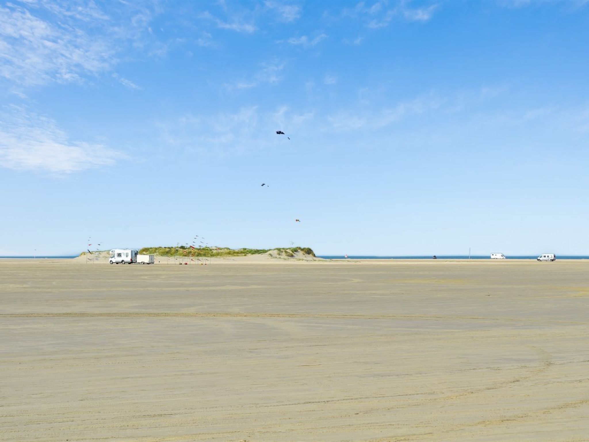 Ein weiter, offener Strand mit einigen Fahrzeugen und einem kleinen Gebäude in der Ferne.