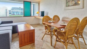 A dining area with a wooden table and wicker chairs, a sofa, and a TV on a stand.