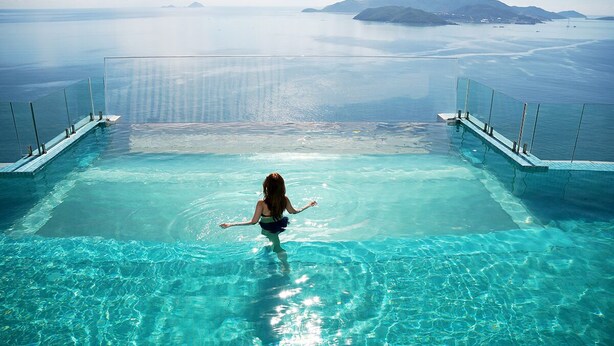 A person standing in a clear blue infinity pool with glass railings, overlooking a calm sea and distant islands. - Zahoo house in Panorama Nha Trang  (Nha Trang)