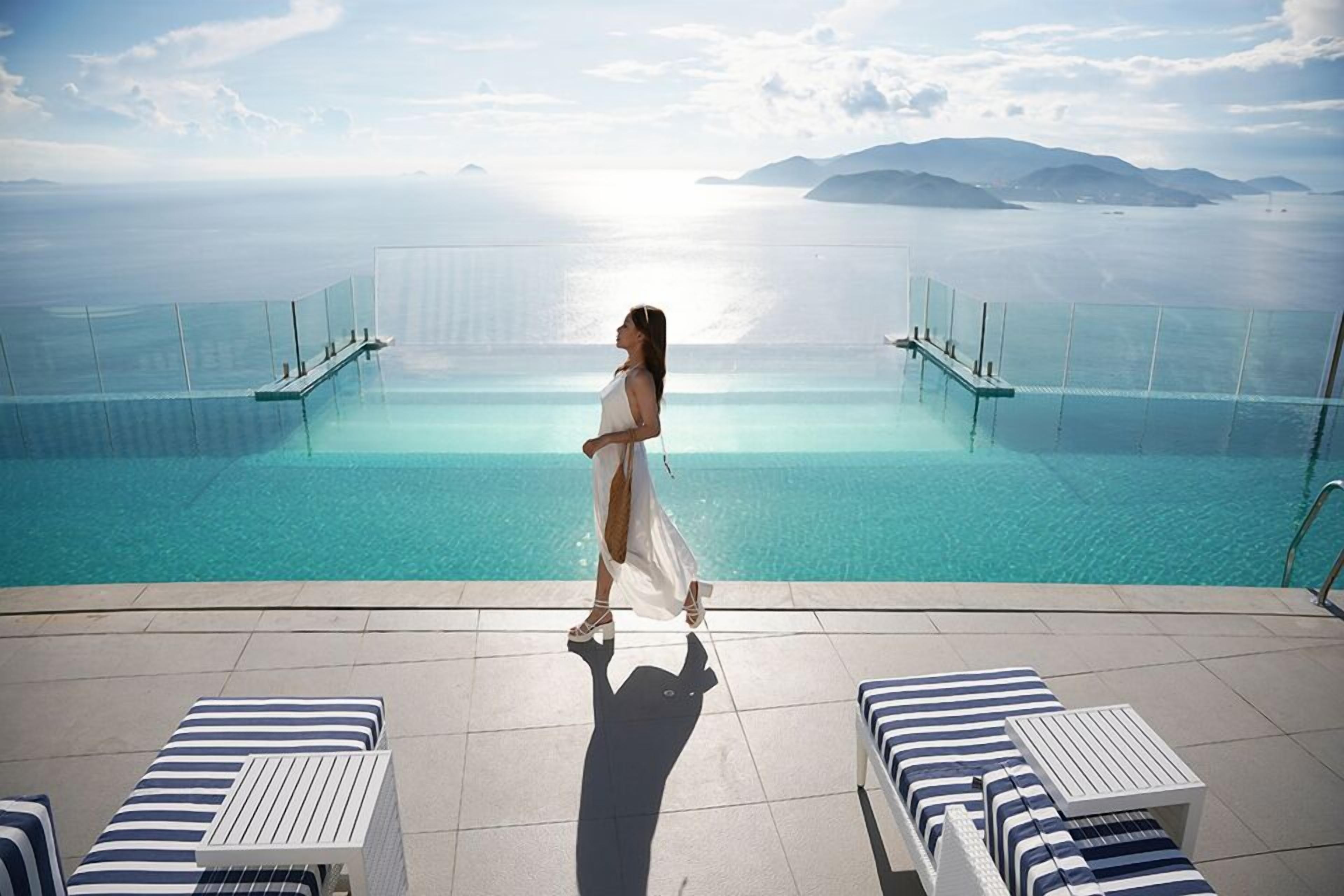 A woman walking towards a infinity pool with a clear view of the sea and distant islands.