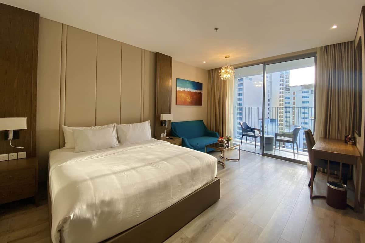 Ein modernes Hotelzimmer mit einem großen Bett, einem blauen Sessel, einem kleinen Tisch und einem Balkon mit Blick auf die Stadt.