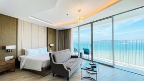 A modern hotel room with a bed, a sofa, a small table, and a balcony with a view of the sea. - Zahoo house in Panorama Nha Trang  (Nha Trang)