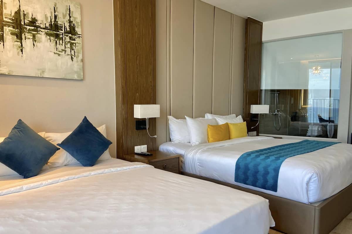 Ein Hotelzimmer mit zwei Betten, einem großen Gemälde an der Wand, einer Wandverkleidung aus Holz und Meerblick durch eine Glastür.