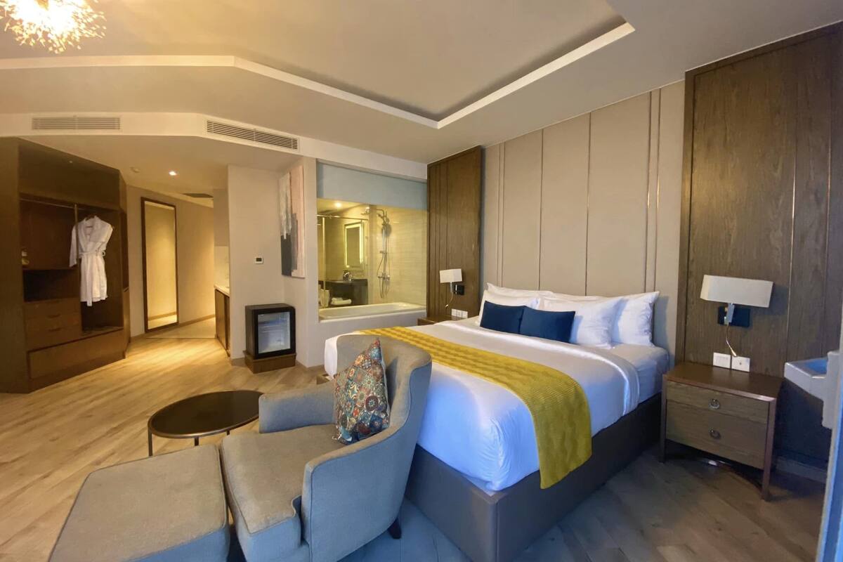 Ein modernes Hotelzimmer mit einem großen Bett, Nachttischen, einem Sessel, einem Schreibtisch, einem Spiegel und einem begehbaren Kleiderschrank.