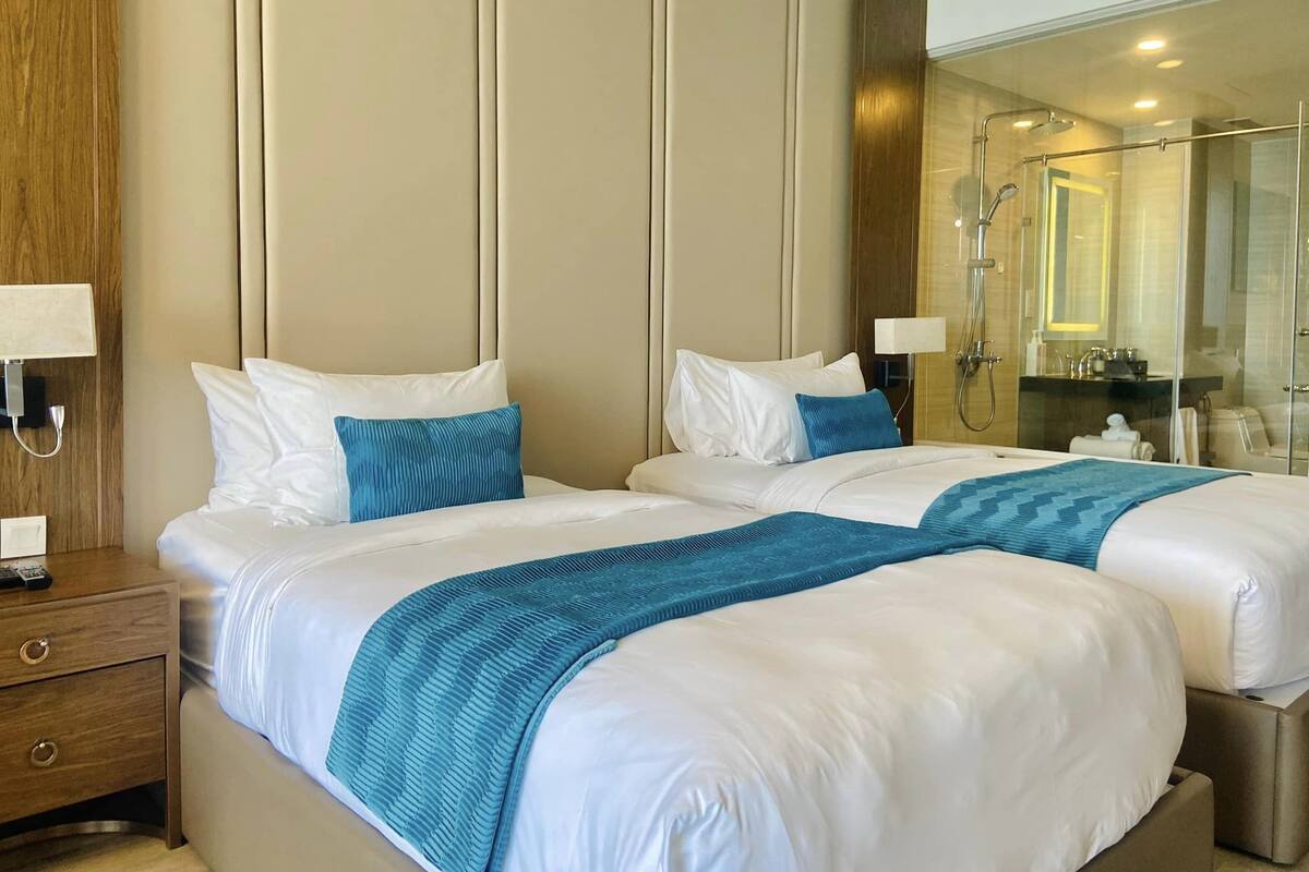 Ein Hotelzimmer mit zwei Betten, einem Holfnachtschränkchen, einem Spiegel und einer Duschkabine aus Glas.