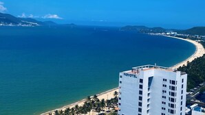 A high-rise hotel with a view of a curved beach and ocean. - Zahoo house in Panorama Nha Trang  (Nha Trang)