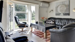 Sala de estar moderna com sofá de couro, mesa de jantar e uma cadeira. Uma grande janela oferece vista para o exterior.