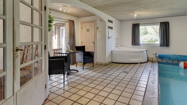 Quarto com piso de azulejos, banheira, janela com cortinas e porta com painéis de vidro.