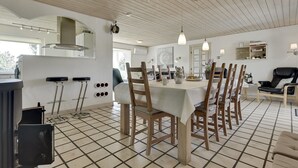 Uma sala de jantar com uma mesa grande, cadeiras de madeira e piso ladrilhado.