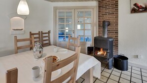 Uma área de refeições acolhedora com uma mesa posta para dois, lareira e vista através de uma porta de vidro.