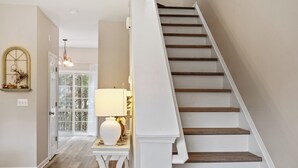 A staircase with wooden steps and white walls, leading to a room with a lamp and a decorative mirror. - Amazing Location Near Cary/Morrisville/Apex Downtown, Close to RDU/RTP/ Shopping (Cary)