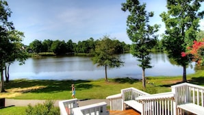 A wooden deck with white railings overlooking a calm lake, surrounded by trees and greenery. - Amazing Location Near Cary/Morrisville/Apex Downtown, Close to RDU/RTP/ Shopping (Cary)