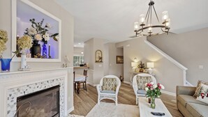 A living room with a fireplace, white armchairs, a sofa, and a chandelier. - Amazing Location Near Cary/Morrisville/Apex Downtown, Close to RDU/RTP/ Shopping (Cary)
