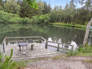 Eine Holzsteg mit Tisch und Stühlen mit Blick auf einen stillen See, umgeben von dichtem Wald.