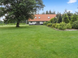 Ein Haus mit rotem Ziegeldach, umgeben von einem gepflegten Rasen und verschiedenen Sträuchern.