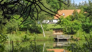 A serene lakeside view with a wooden dock extending into the water, surrounded by lush greenery and a house with a red roof in the background. - "Beatha" - 25km to the fjord by Interhome (Sønder Felding)