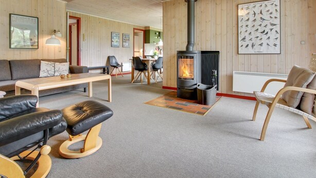 Ein gemütliches Wohnzimmer mit Kaminofen in der Mitte, einem Essbereich und einer Sitzecke mit Sofa und Sesseln.