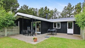 Ein modernes Haus mit überdachter Terrasse, Essbereich und Garten.