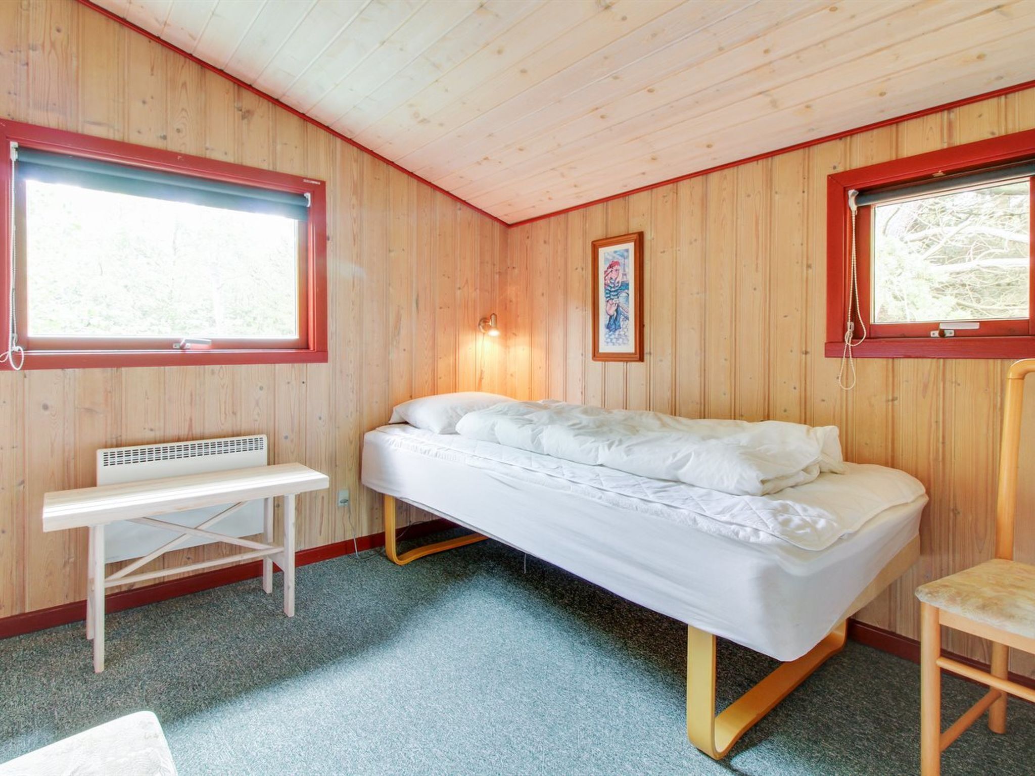 A single-bed room with wooden walls, a bench, a bedside table, and two windows with blinds.