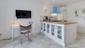 Een moderne keuken met een centraal eiland, witte kasten, een flatscreen televisie en een eethoek met een stoel.