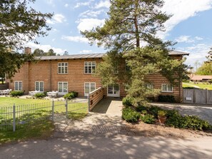A two-story brick building with a covered patio area, a fenced garden, and a gravel driveway.