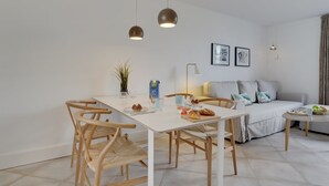 Een moderne, goed verlichte kamer met een eettafel, stoelen, een bank en een bed.