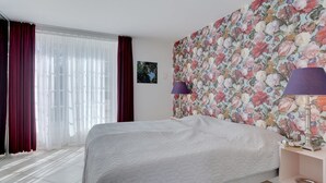 Een hotelkamer met een groot bed, een nachtkastje met een lamp en bloemenbehang.